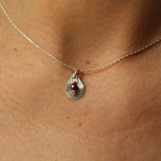 Necklace with a teardrop pendant featuring a garnet gemstone on a person's neck.