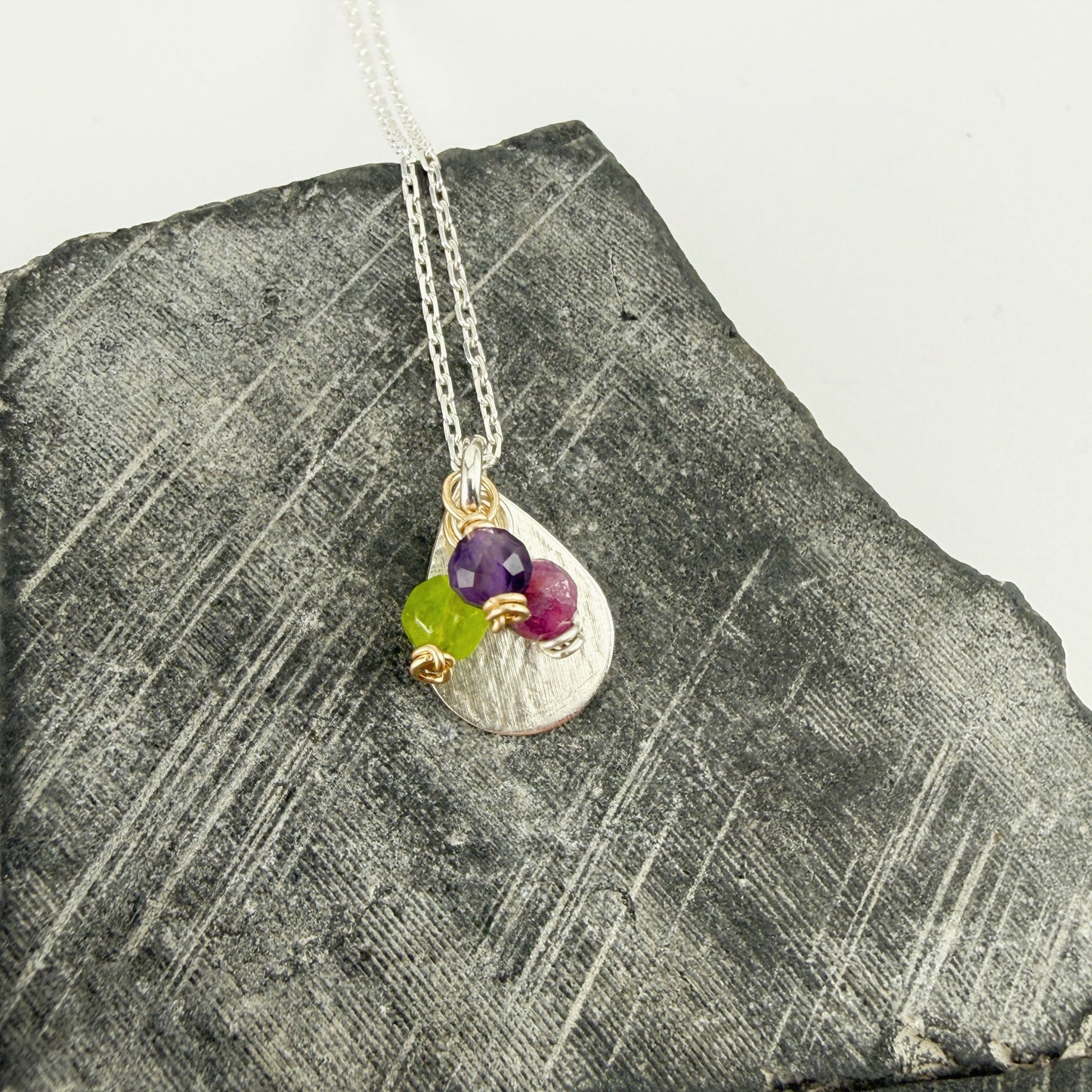 Silver necklace with 3 birthstone charms on a gray stone surface