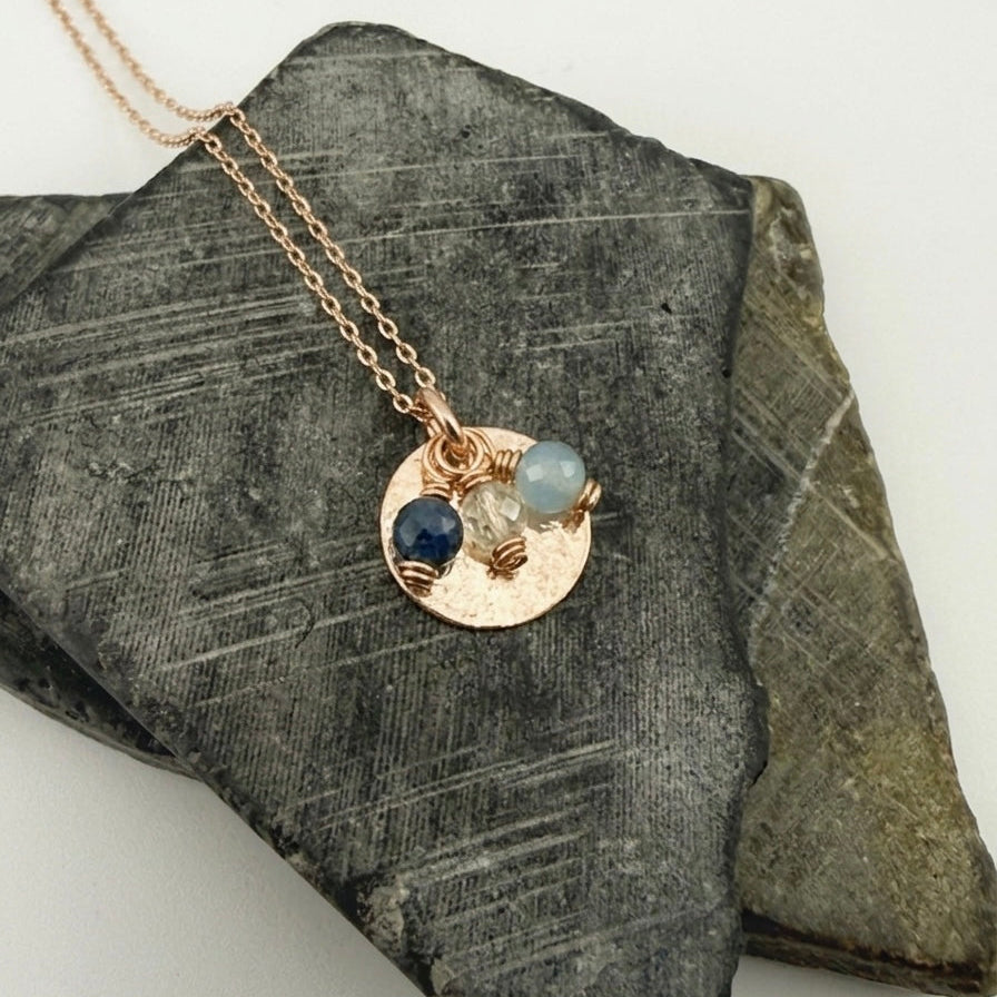 Gold necklace with birthstone charms and a circle pendant on a dark stone surface