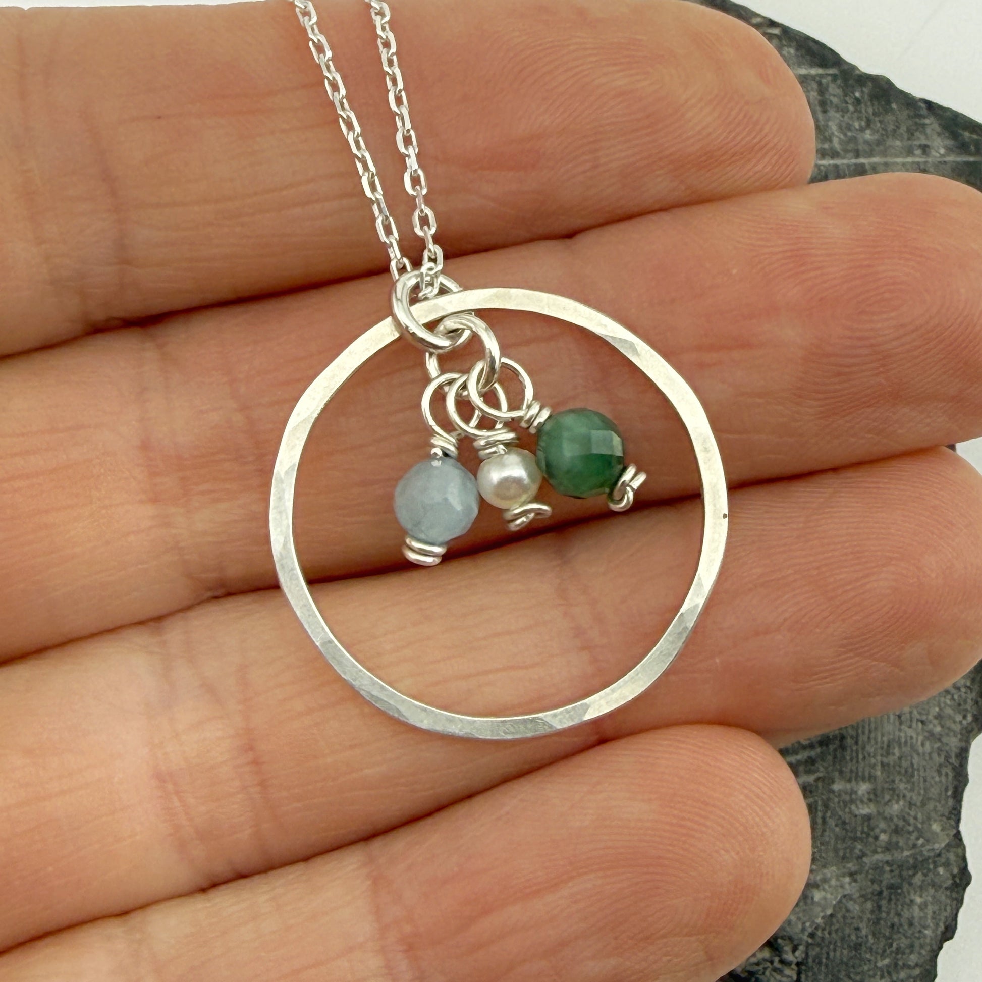 Silver necklace with circular pendant and birthstones held between fingers on a white background