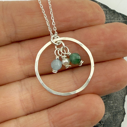 Silver necklace with circular pendant and birthstones held between fingers on a white background