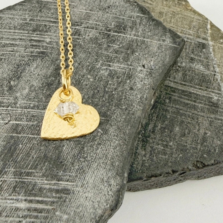 Gold heart-shaped necklace with a pendant and diamond birthstone charm on a textured stone surface