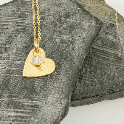 Gold heart-shaped necklace with a pendant and diamond birthstone charm on a textured stone surface