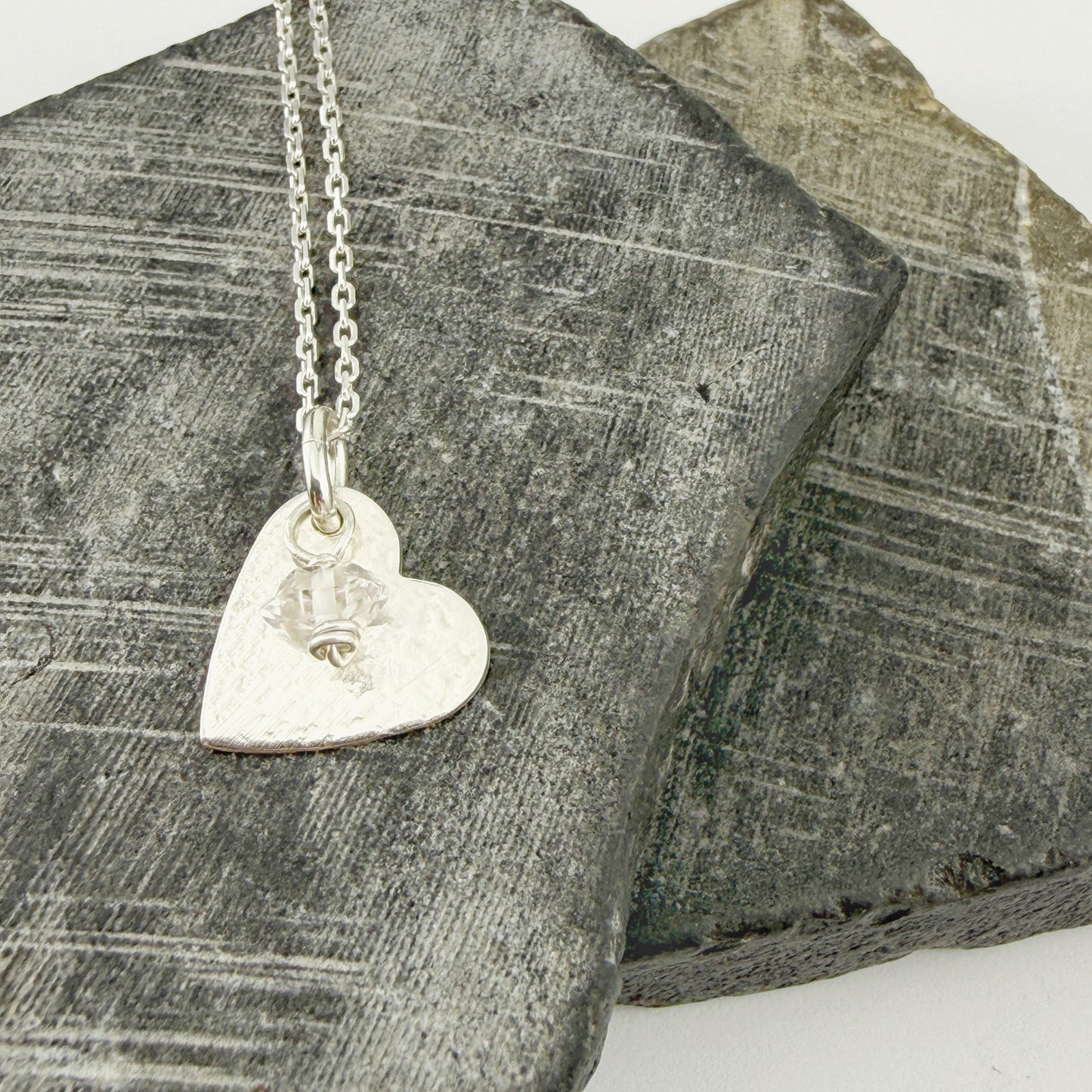Silver heart-shaped pendant necklace with custom birthstone charm on a textured stone surface