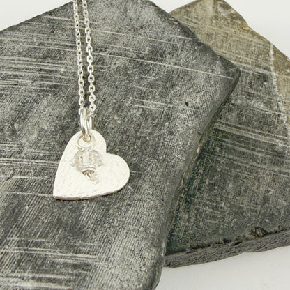 Silver heart-shaped pendant necklace with custom birthstone charm on a textured stone surface