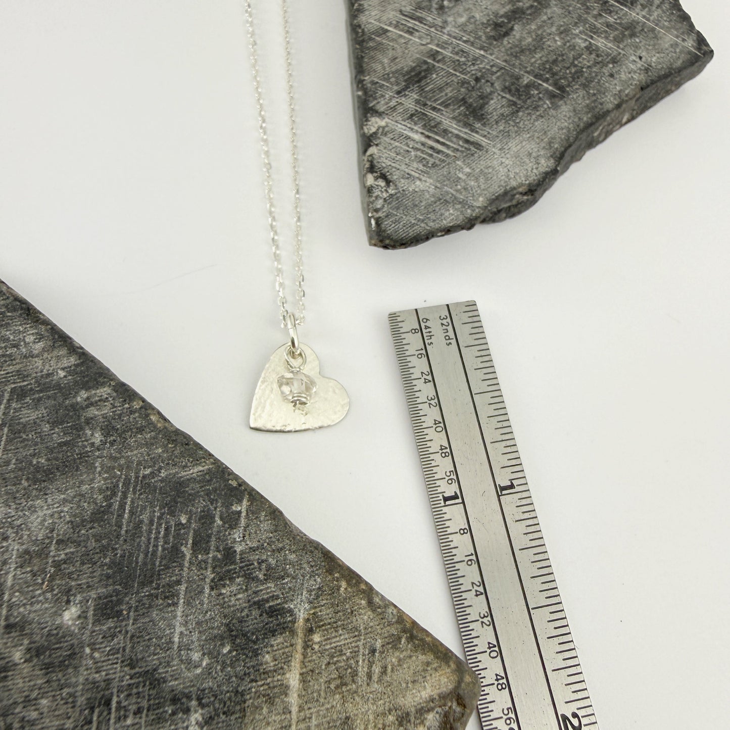 Dainty sterling silver necklace with a heart pendant on a textured surface next to a ruler for scale.