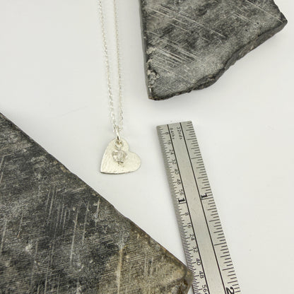 Dainty sterling silver necklace with a heart pendant on a textured surface next to a ruler for scale.