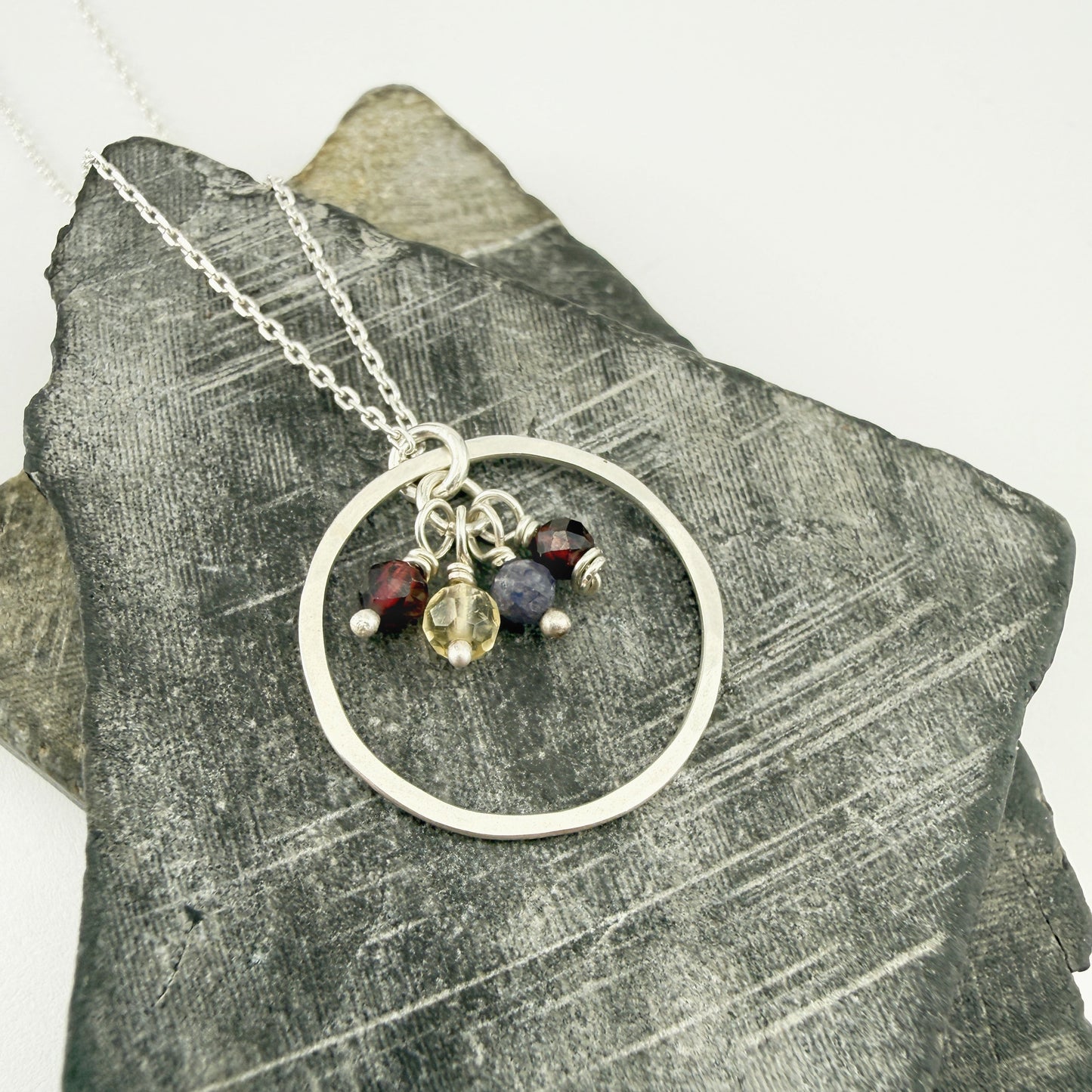 Silver necklace with circular pendant and birthstone charms on a textured stone surface