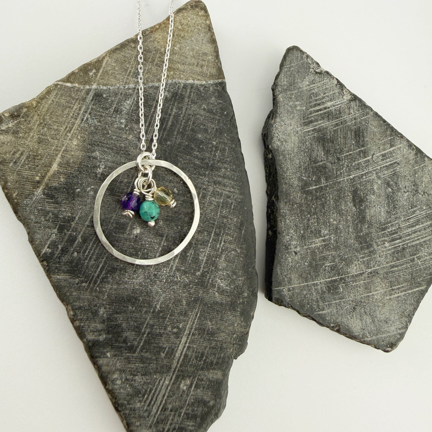 Necklace with circular pendant and three birthstone charms on a stone surface