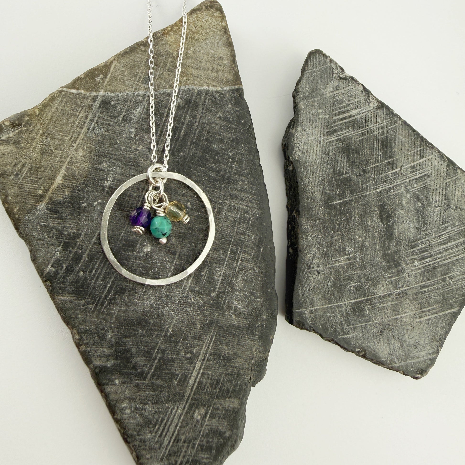 Necklace with circular pendant and three birthstone charms on a stone surface