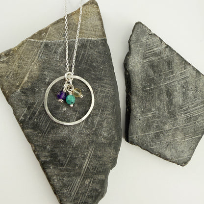 Necklace with circular pendant and three birthstone charms on a stone surface