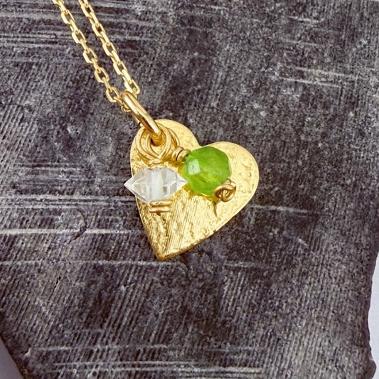 Gold heart-shaped pendant with gemstones for with August and April birthstones on a textured surface