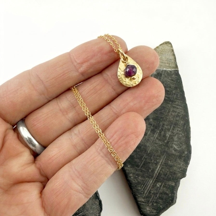 Gold necklace with a pendant held by a hand, next to dark stone on a white background