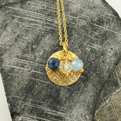 Gold necklace and pendant with custom birthstone charms on a textured stone surface