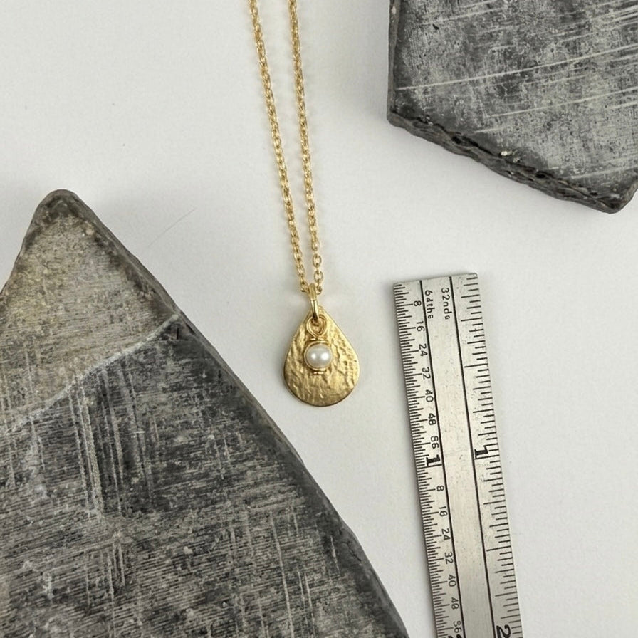 Gold necklace with a pendant on a white surface next to a ruler for scale.