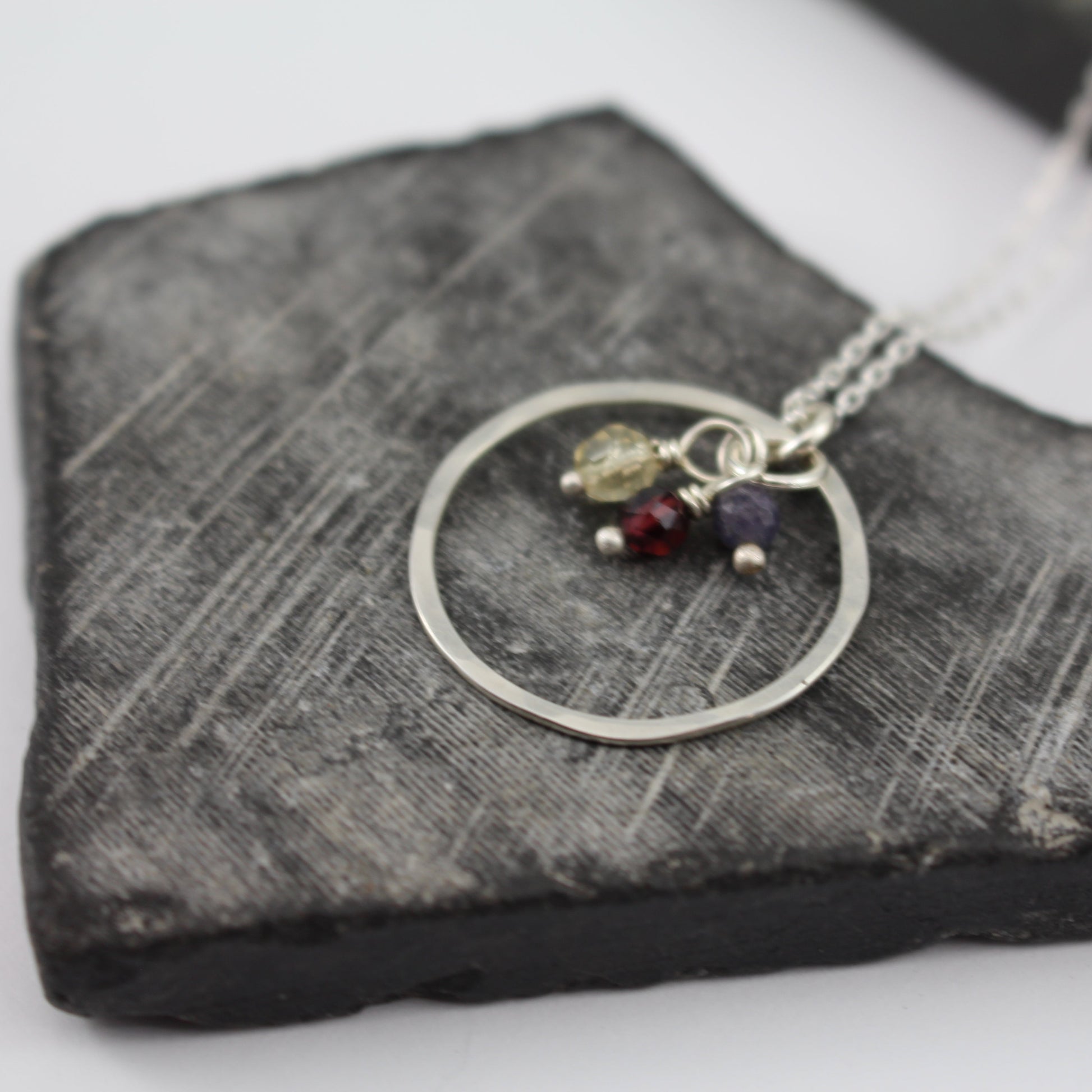 Hammered silver necklace with circular pendant and small stones on a textured stone surface