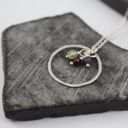 Hammered silver necklace with circular pendant and small stones on a textured stone surface