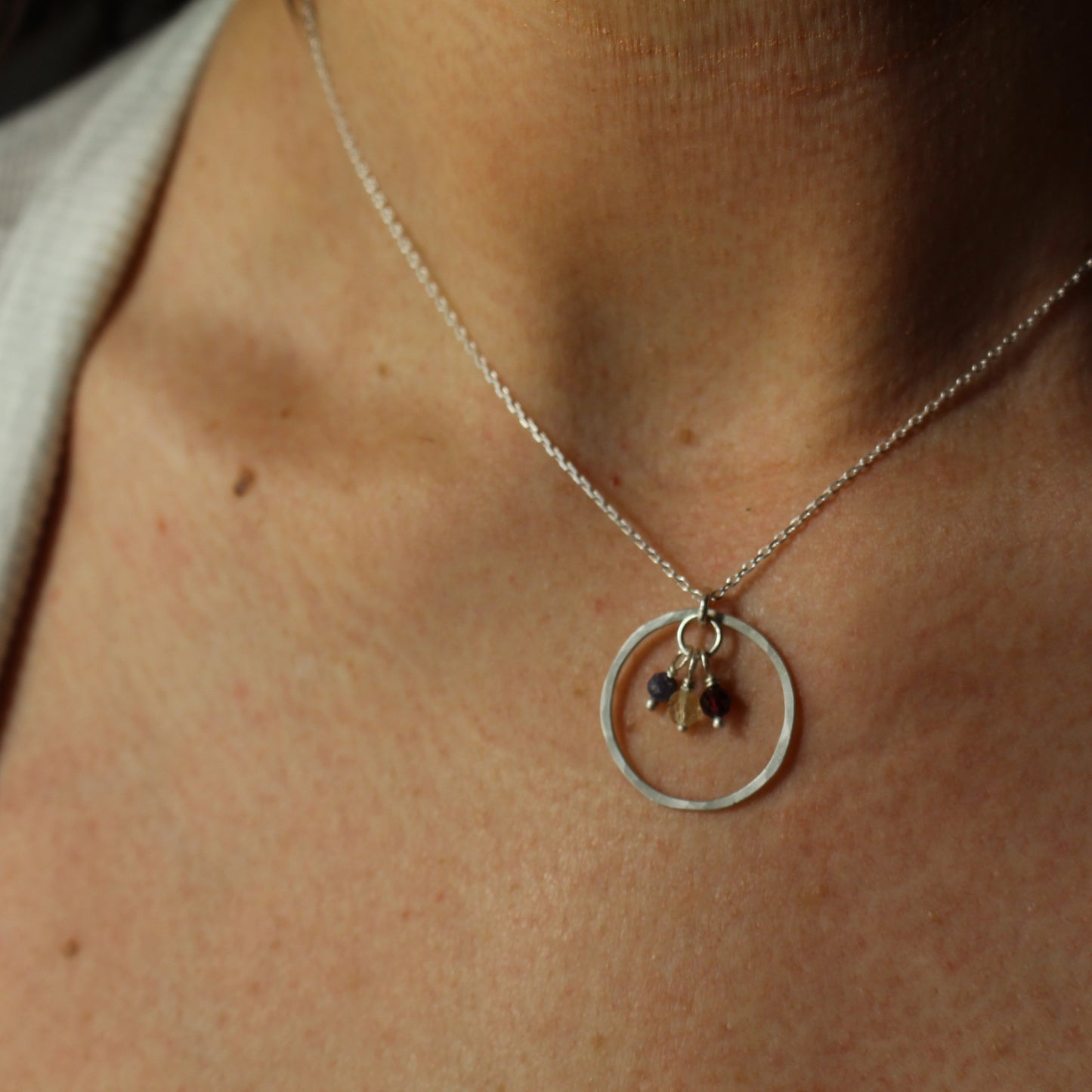 Keepsake necklace with a circular pendantand birthsstones in silver on a person's neck