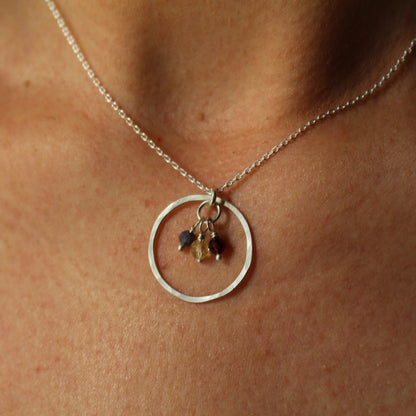 Silver necklace with a circular pendant and hanging birthstone charms on a person's neck