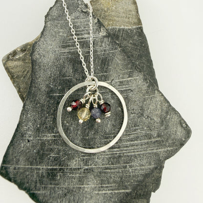Necklace with a silver circular pendant and birthstones on a textured stone surface