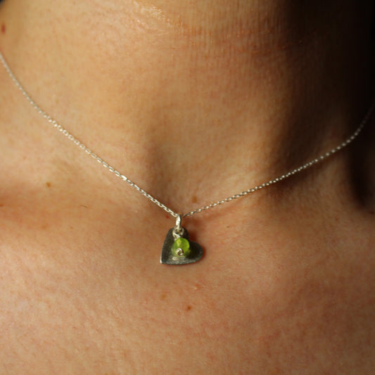 Necklace with a silver heart and Peridot charm  worn by a person