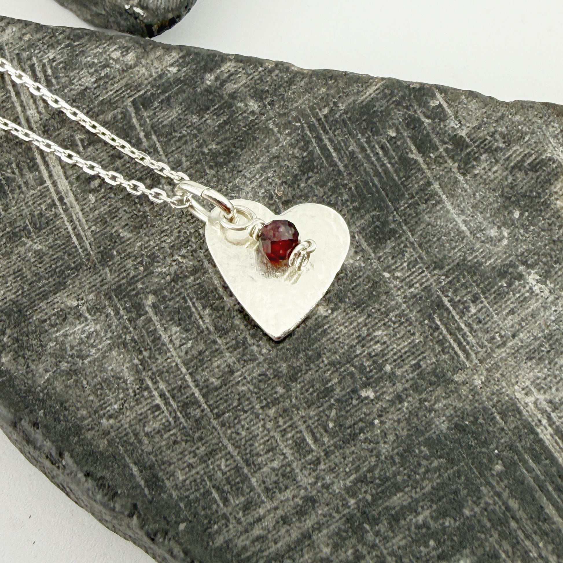 Silver heart-shaped necklace with a January garnet birthstone charm on a textured stone surface