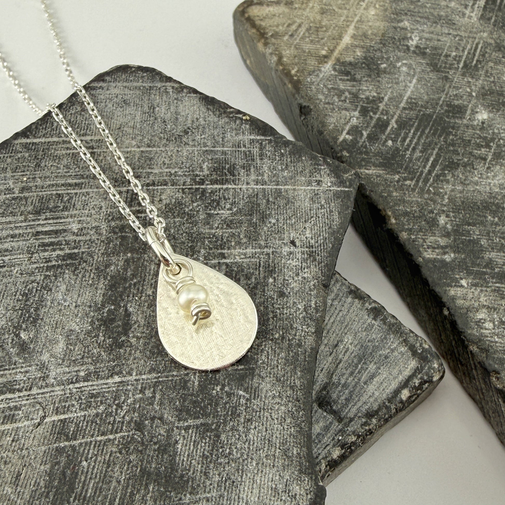 Silver necklace with a teardrop pendant and pearl charm on a textured stone surface
