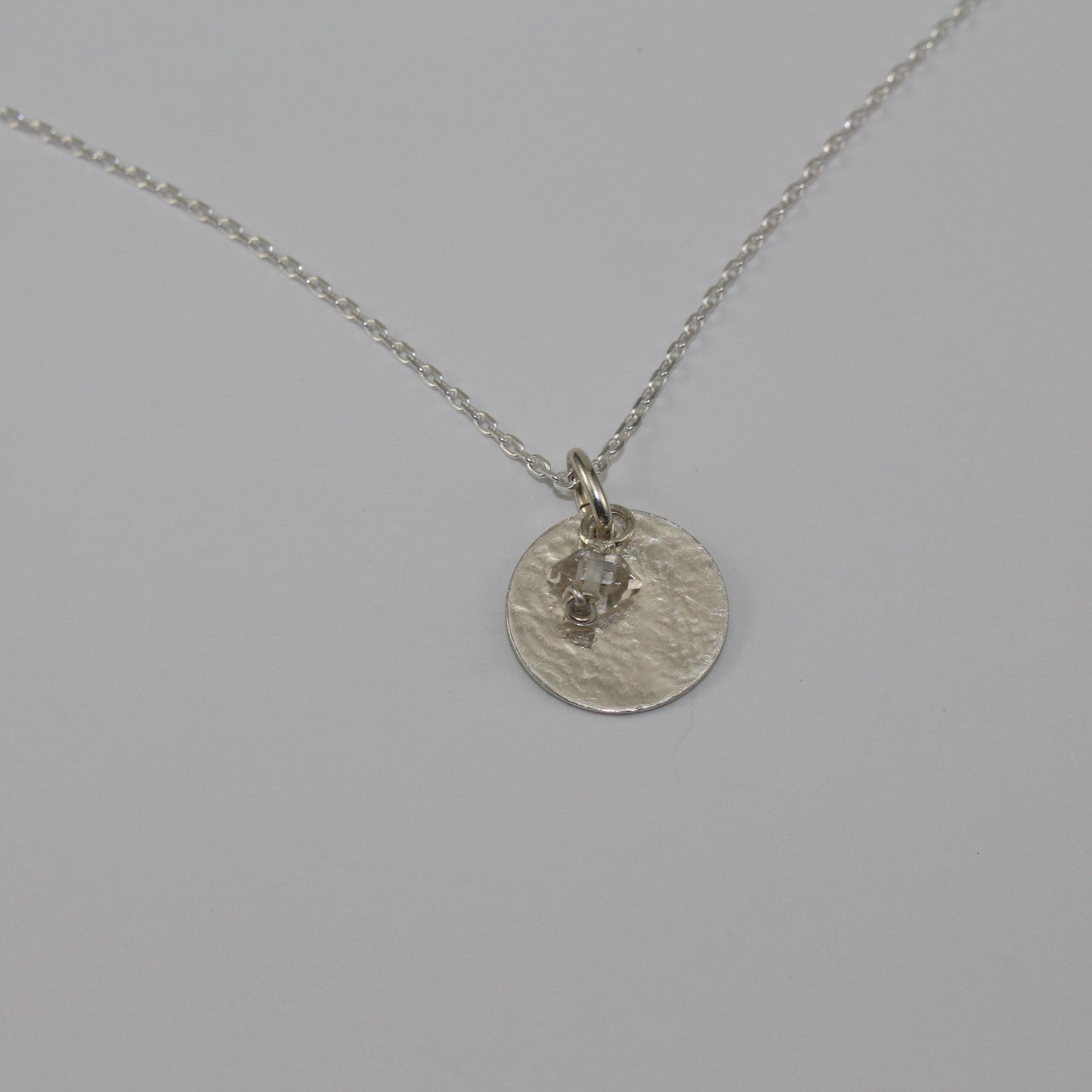 Silver necklace with a round pendant and herkimer diamond birthstone on a light gray background