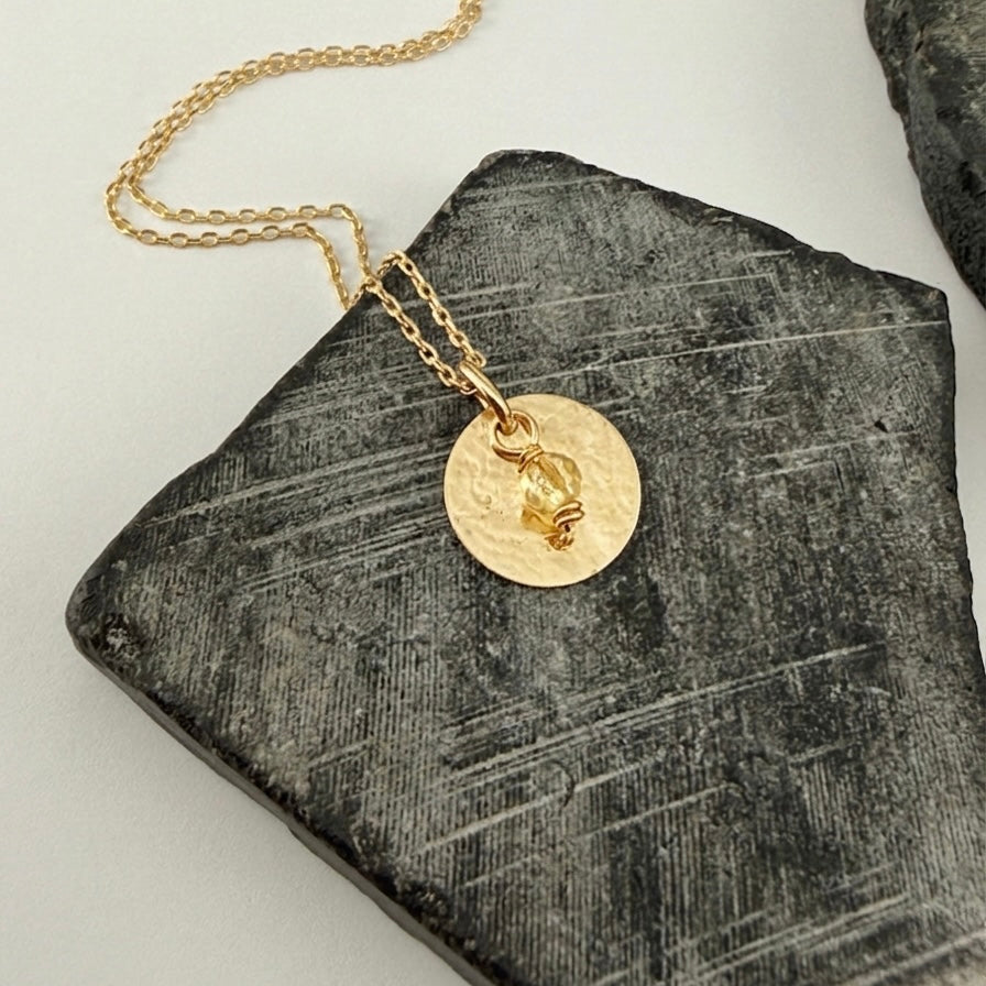 Yellow Gold and Citrine Birthstone Pendant Necklace on a textured stone surface