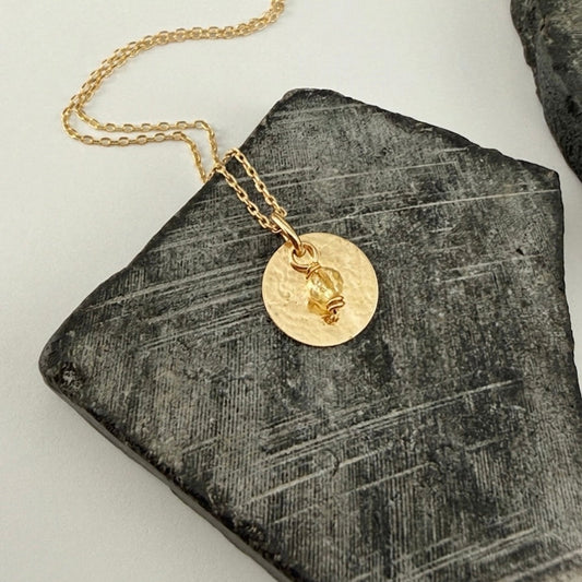 Yellow Gold and Citrine Birthstone Pendant Necklace on a textured stone surface