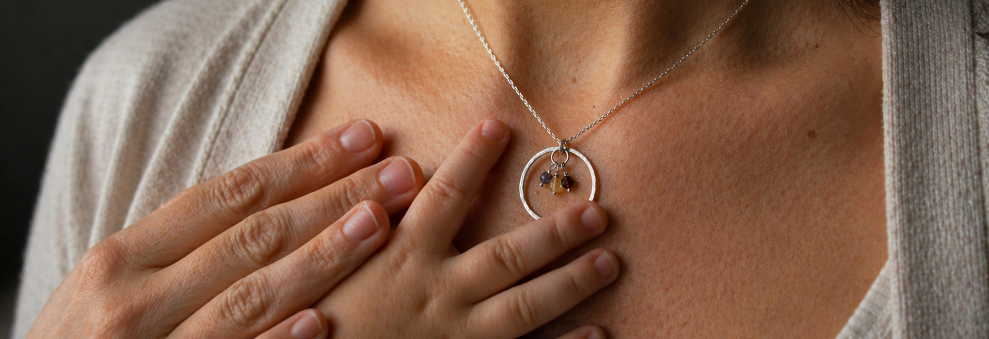 Mother with silver pendant necklace and birthstone charms, small baby's hand reaching for the necklace